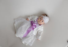 Lade das Bild in den Galerie-Viewer, Babydirndl Taufkleid von Anna Kaval in Flieder mit Bolero, präsentiert auf einem Baby, das in einem eleganten weißen Kleid mit lila Schleife und floralen Akzenten liegt.