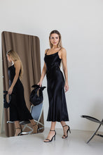 Lade das Bild in den Galerie-Viewer, Frau trägt elegantes schwarzes Satin-Midikleid aus 100% Viskose mit Spaghettiträgern und Wasserfall-Ausschnitt