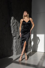 Lade das Bild in den Galerie-Viewer, Frau trägt ein elegantes schwarzes Wickel-Abendkleid mit Schlitz und feinen Trägern in einem modernen