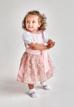 Lade das Bild in den Galerie-Viewer, Ein fröhliches Kind zeigt das Taufdirndl Traum aus Seide von Anna Kaval, mit süßem Design und verspielter Schürze.