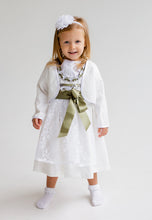 Lade das Bild in den Galerie-Viewer, Lächelndes kleines Mädchen in einem zauberhaften Babydirndl mit Bolero von Anna Kaval, perfekt für Taufen und Feierlichkeiten. Das Kleid in zartem Elfenbeinton mit grüner Satinbindung.