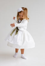 Lade das Bild in den Galerie-Viewer, Ein kleines Mädchen in einem weißen Babydirndl von Anna Kaval, mit Bolero und grünem Satinband, das voller Freude im Zickzack tanzt. Perfekt für Taufen und besondere Anlässe.