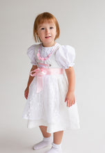 Lade das Bild in den Galerie-Viewer, Ein fröhliches Mädchen trägt das Babydirndl/Taufdirndl/Taufkleid Rosalie von Anna Kaval, perfekt für festliche Anlässe. Das bezaubernde Taufkleid Mädchen überzeugt mit einem weißen Jacquard-Stoff und süßen Puffärmeln. Ideal als Taufdirndl.