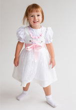 Lade das Bild in den Galerie-Viewer, Das Babydirndl/Taufdirndl/Taufkleid Rosalie von Anna Kaval zeigt ein lachendes Mädchen, das in einem eleganten weißen Kleid mit rosa Akzenten gekleidet ist. Dieses Taufkleid Mädchen ist eine wunderbare Wahl für besondere Anlässe und eignet sich hervorragend als Taufdirndl.
