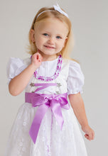 Lade das Bild in den Galerie-Viewer, Ein strahlendes Lächeln eines Mädchens in einem Babydirndl von Anna Kaval. Dieses Flieder Taufdirndl hat eine wunderschöne Verzierung und macht jeden Anlass unvergesslich.