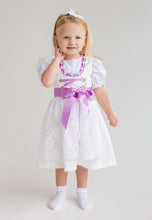 Lade das Bild in den Galerie-Viewer, Ein kleines Mädchen in einem bezaubernden Babydirndl von Anna Kaval. Das Kleid in Fliederfarbe hat eine hübsche Schnürung und eine zarte Schürze aus Spitzestoff. Ideal für Taufen und Feste, dieses Taufdirndl sorgt für einen eleganten Auftritt.