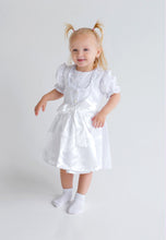 Lade das Bild in den Galerie-Viewer, Ein kleines Mädchen trägt ein bezauberndes Baby Trachtenkleid zur Taufe von Anna Kaval, gefertigt aus Bio-Baumwolle, mit einer eleganten Bluse und Schürze.