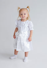 Lade das Bild in den Galerie-Viewer, Bezauberndes Baby Trachtenkleid zur Taufe von Anna Kaval, ein kleines Mädchen in einem eleganten weißen Kleid mit Rüschendetails und Satinband.