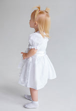 Lade das Bild in den Galerie-Viewer, Bezauberndes Baby Trachtenkleid zur Taufe von Anna Kaval, ein kleines Mädchen von der Seite in einem stilvollen weißen Kleid mit Satinband.